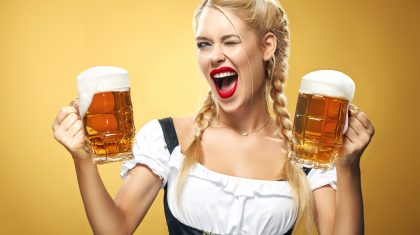 Half-length portrait of young sexy blonde with big breast wearing black dirndl with white blouse holding the beer mug Isolated on dark background