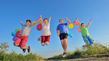 happy children jumping on field with balloons in summer time