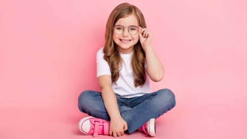 Photo of dream funny little girl sit floor wear glasses white t-shirt jeans shoes isolated pink color background