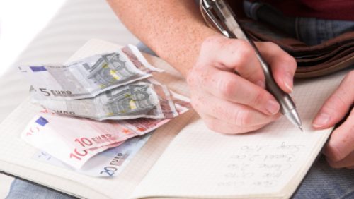 Womanhand writing down the expenses paid while some euro bills are lying on her household book